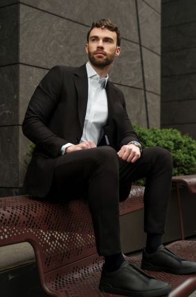 Man in a suit sitting on a bench against a building.