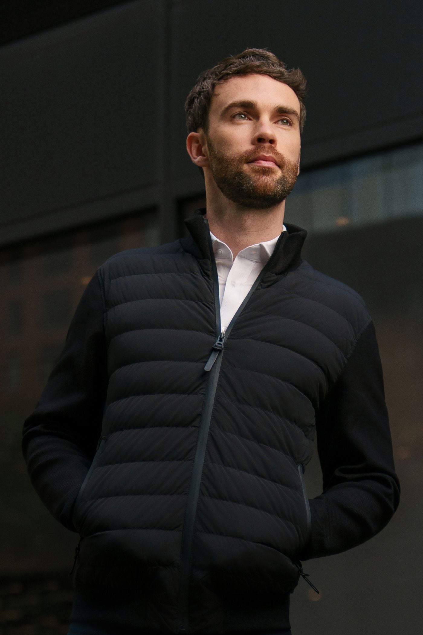 Man wearing a black puffer vest over a white shirt against a dark background